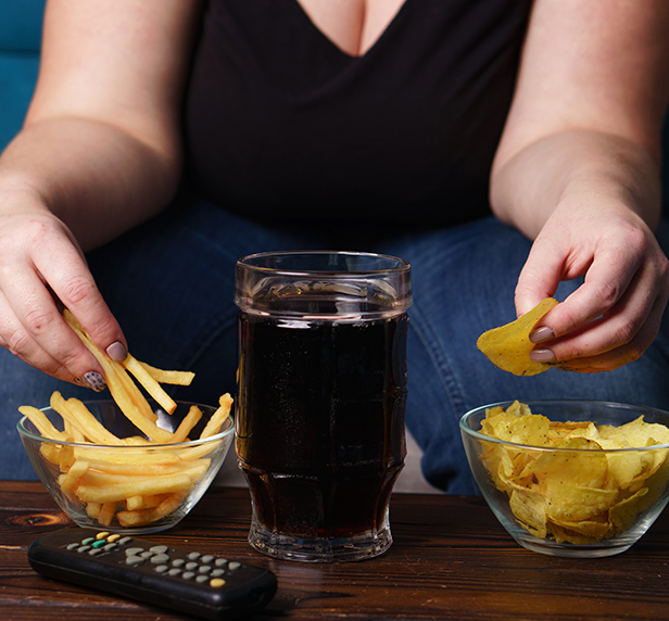 A woman with a large coke and a bowl of fries, and potato chips suffering from Binge Eating Disorder