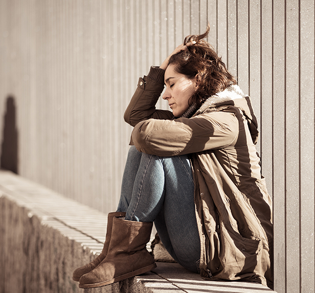 A woman sits outside and puts her hand in her hair, she's worried about her substance abuse.